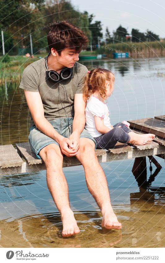 Young boy and his little sister sitting on jetty over the lake and dipping feet in water on sunny day in the summertime Lifestyle Joy Happy Relaxation