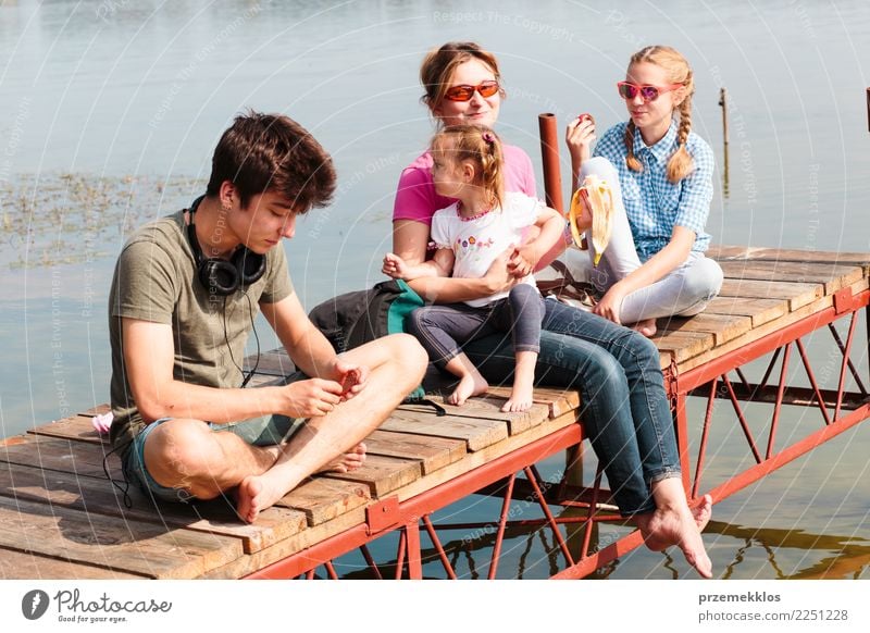 Family spending vacation time together having a snack sitting on jetty over the lake on sunny day in the summertime Joy Happy Relaxation Leisure and hobbies