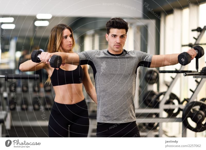 Female personal trainer helping a young man lift dumbells Lifestyle Body Sports Human being Masculine Feminine Young woman Youth (Young adults) Young man Woman