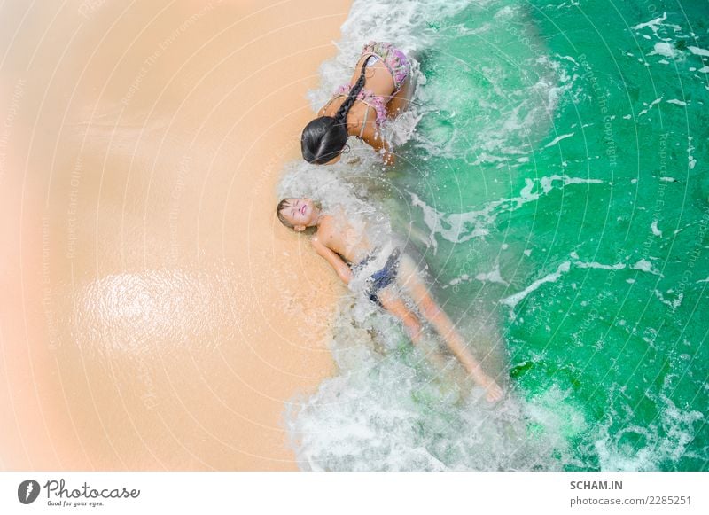 Cute boy and girl having fun on the sunny tropical beach. Lying on sand, wonderful waves around them. View from above. Vibrant color concept, copy space. Joy