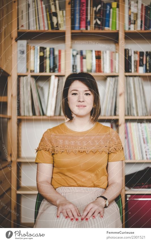 Young woman sitting on a chair (with a bookshelf behind her) Harmonious Well-being Contentment Feminine Youth (Young adults) Woman Adults 1 Human being