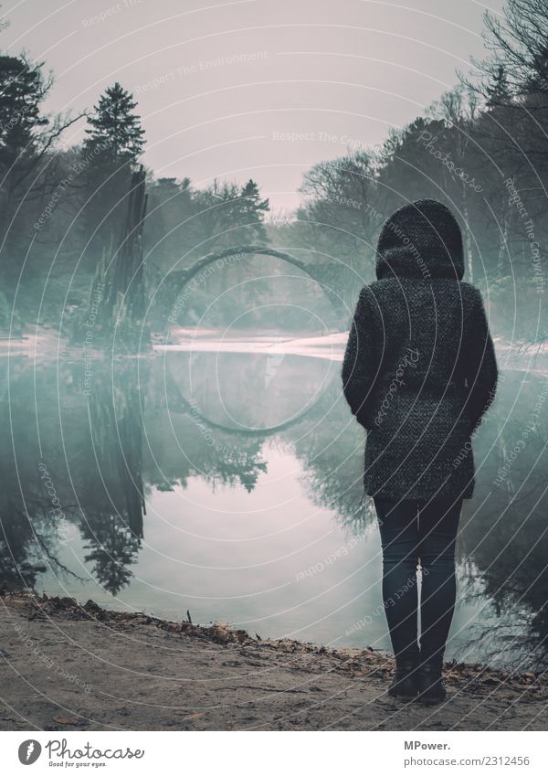 woman at the lake before bridge Human being 1 Environment Nature Park Old Bridge Mystic Woman Stand Lake Reflection Shroud of fog Gloomy Hooded jacket