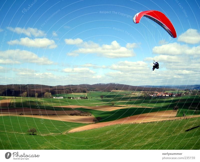 Paraglider with red paraglider flies over green meadows and fields against a sky with clouds Paragliding Adventure Freedom Sportsperson Skydiving Flying