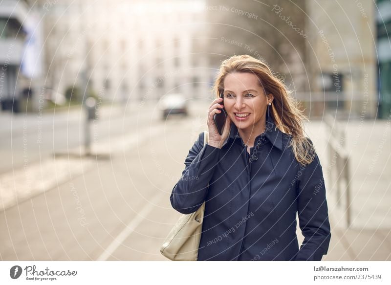 Attractive blond woman chatting on her smartphone Happy Face Business To talk Telephone Cellphone PDA Technology Woman Adults 1 Human being 45 - 60 years Street