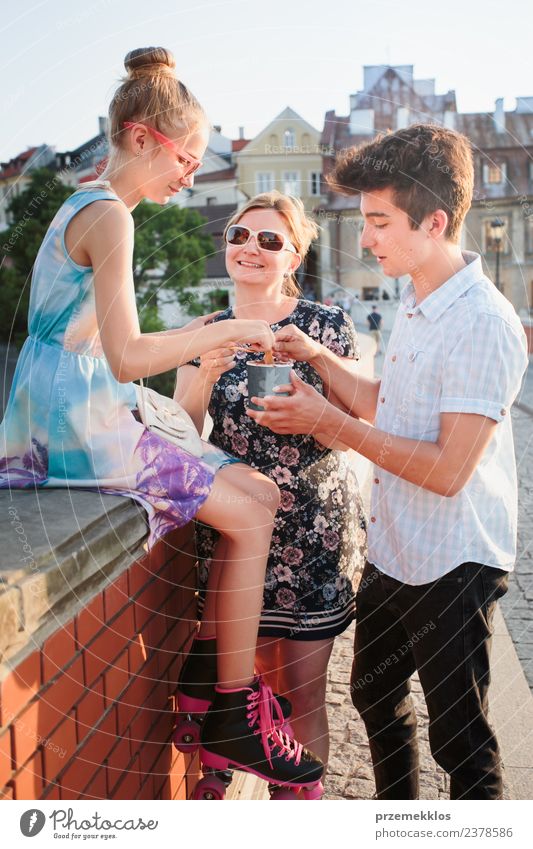 Family spending time together in the city centre enjoy eating ice cream on a summer day. Mother, teenage girl and boy spending quality time on sunny afternoon eating sweet dessert. Downtown area, old town in the background