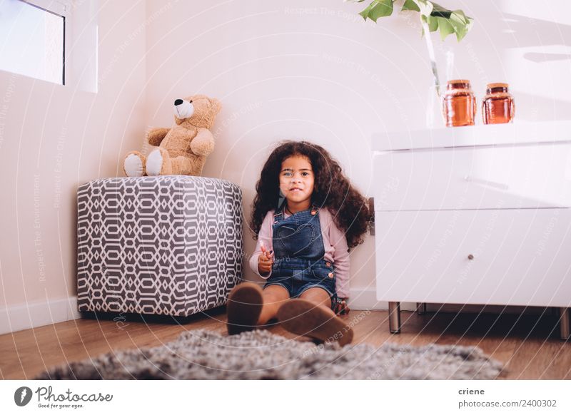 little afrcian girl is holding a lollipop sitting on the floor Happy Beautiful Child Plant Boots Toys Teddy bear Smiling Sit Small Cute Bear Home room kid