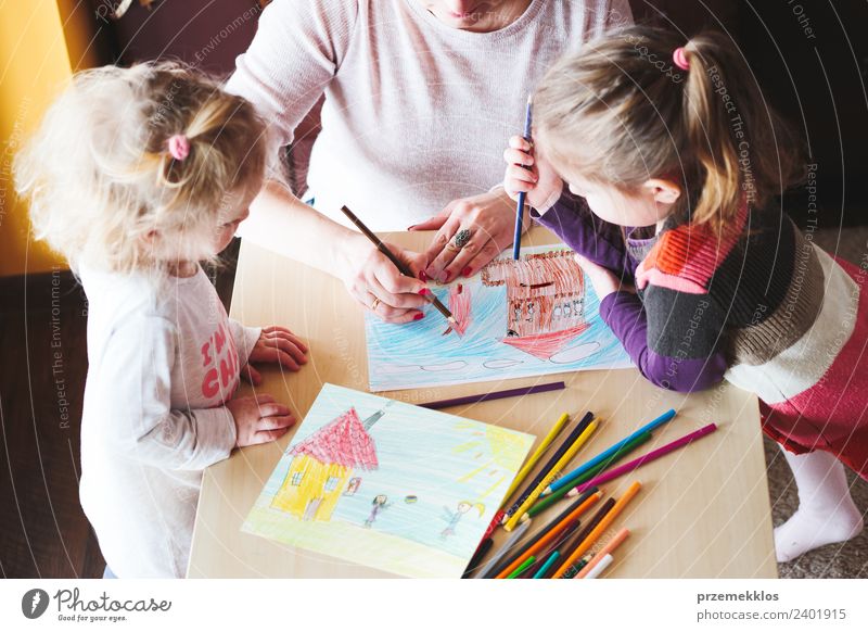 Mom with little girls drawing a colourful pictures of house and playing children using pencil crayons standing at table indoors Lifestyle Joy Happy Handcrafts