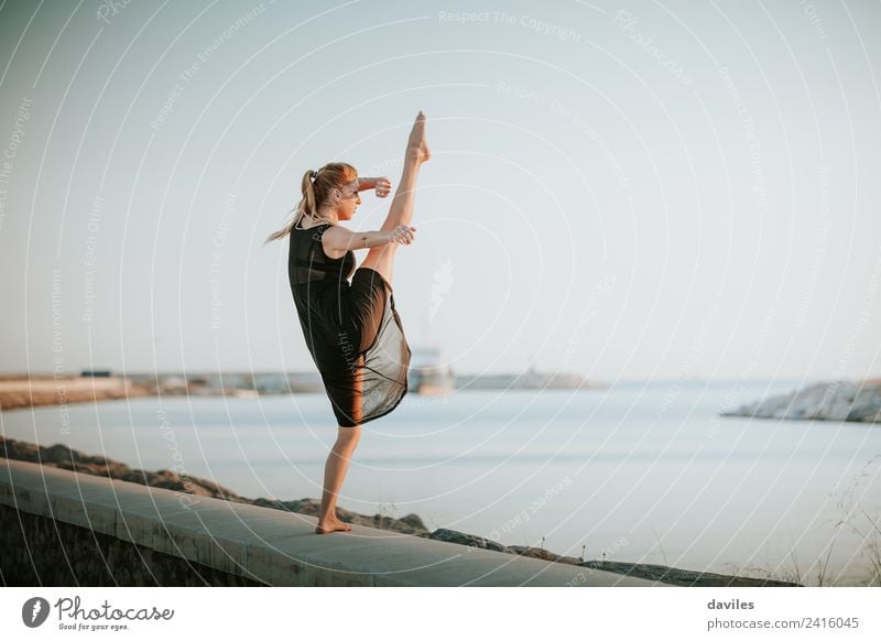 Young dancer in black dress raising up a leg, outdoors, with the sea in the background. Lifestyle Joy Body Vacation & Travel Ocean Dance Sports Human being