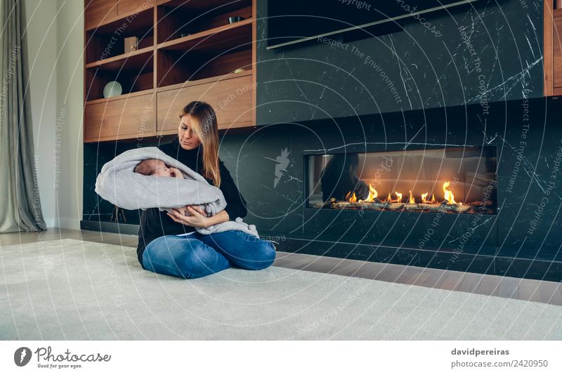 Young mother hugging her newborn baby in front of fireplace Lifestyle Happy Beautiful Furniture Fireside Living room Child Human being Baby Woman Adults Mother