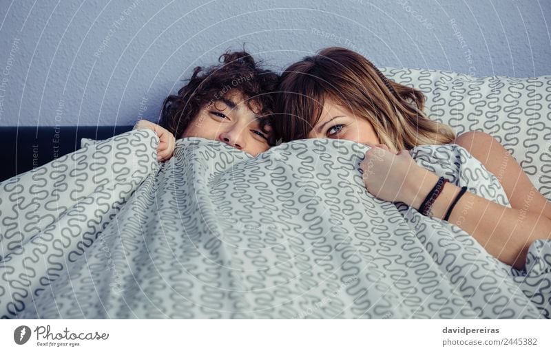 Happy couple laughing and covering mouths under duvet Lifestyle Beautiful Relaxation Bedroom Camera Woman Adults Man Couple Mouth Smiling Laughter Love