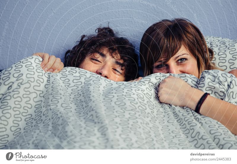 Happy couple laughing and covering mouths under duvet Lifestyle Beautiful Relaxation Bedroom Camera Woman Adults Man Couple Mouth Smiling Laughter Love