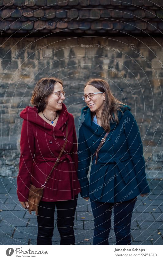 happy twin sisters stand laughing in front of a wall Lifestyle Style Joy luck Human being Feminine Young woman Youth (Young adults) Brothers and sisters Sister