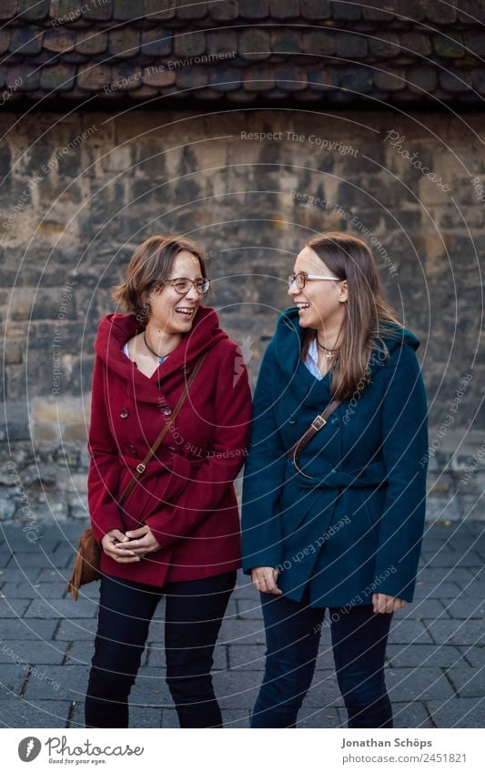 happy twin sisters stand laughing in front of a wall Lifestyle Style Joy luck Human being Feminine Young woman Youth (Young adults) Brothers and sisters Sister