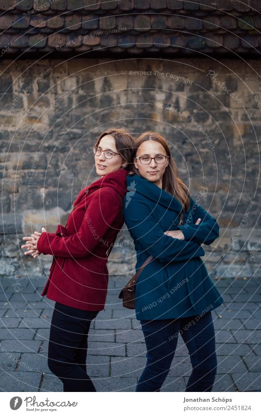 Twin sisters stand cool back to back in front of a wall Lifestyle Style Joy luck Human being Feminine Young woman Youth (Young adults) Brothers and sisters