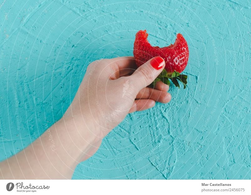 Woman's hand holding a ripe strawberry on blue background. Food Fruit Dessert Nutrition Organic produce Diet Wellness Summer Feminine Adults Skin Hand Nature