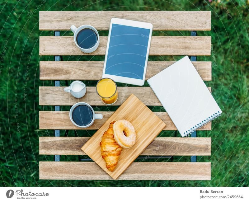 Morning Breakfast In Green Garden With French Croissant, Donuts, Coffee Cup, Orange Juice, Tablet and Notes Book On Wooden Table Background picture White Food