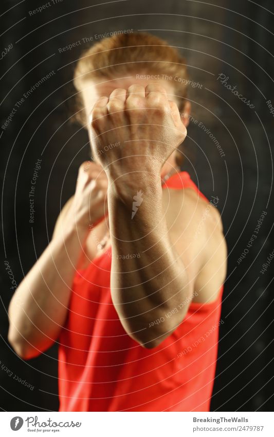 Close up front portrait of one young middle age athletic woman in sportswear in gym over dark background, standing in boxing stance with hands and fists, looking at camera