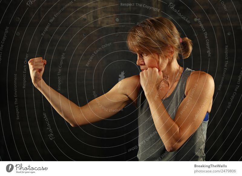 Close up side view profile portrait of one young middle age athletic woman shadow boxing in sportswear in gym over dark background, looking away Lifestyle