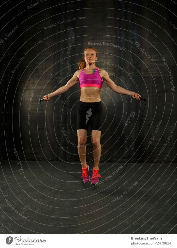 One young middle age athletic, woman training, exercising with fitness jumping rope over dark background, full length front view, looking at camera Lifestyle