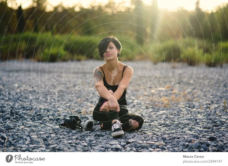 Beautiful young photographer woman wearing black clothes, sitting on the floor in countryside with her camera attractive background backlighting beautiful