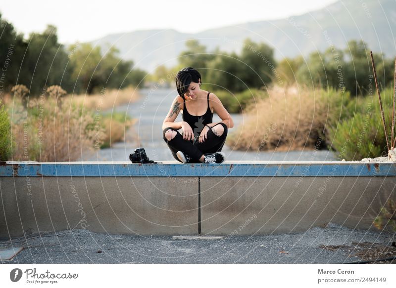 Beautiful young photographer sitting on the ground with the camera in the country Attractive background Background lighting black clothes respiration Brunette