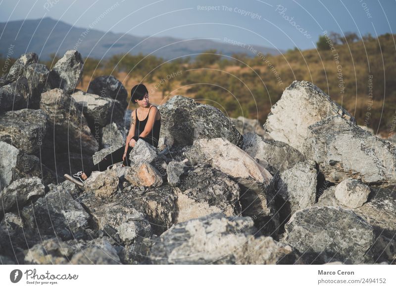 Beautiful young woman thinking and sitting on the rocks outdoors on the countryside attractive background beautiful black clothes brunette camera caucasian day