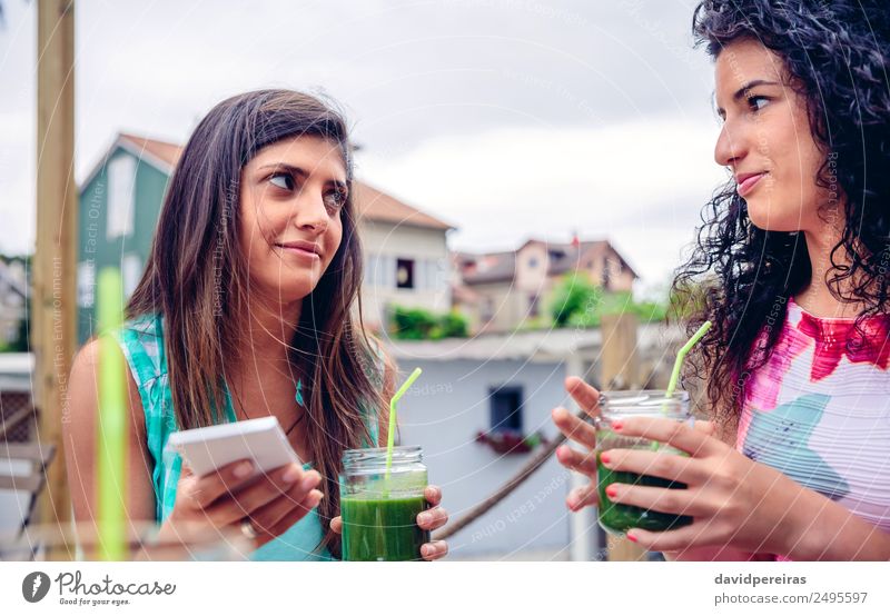 Two women looking at each other and holding green smoothies Vegetable Fruit Nutrition Diet Beverage Juice Lifestyle Happy Summer Telephone PDA Technology