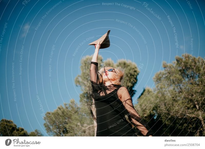 Happy blonde woman raising the arm with a hat in the hand at the forest during sunset. Lifestyle Style Joy Relaxation Vacation & Travel Trip Adventure Freedom