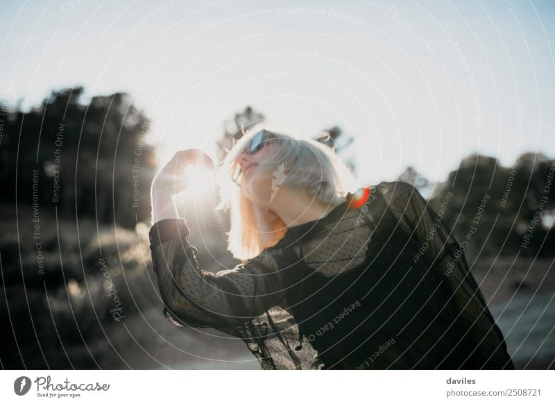 Cool blonde woman with black dress performing dance at sunset, with the sun in the background. Lifestyle Elegant Style Joy Harmonious Sun Human being Feminine