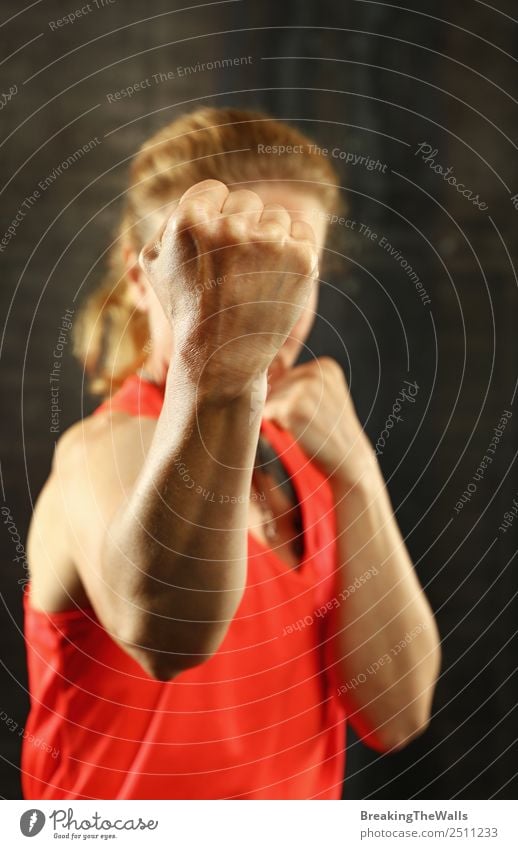 Close up front portrait of one young middle age athletic woman in sportswear in gym over dark background, standing in boxing stance with hands and fists, looking at camera