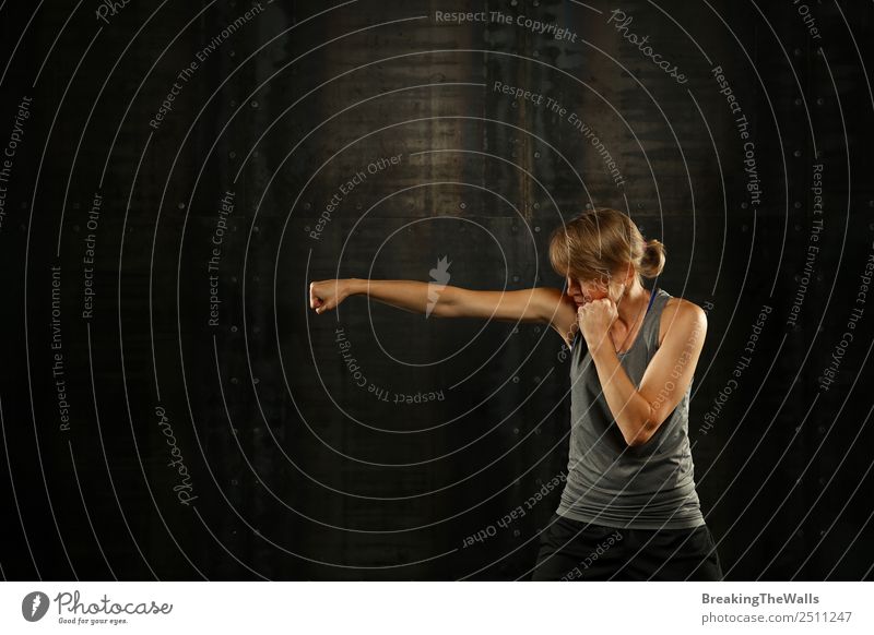 Close up side view profile portrait of one young middle age athletic woman shadow boxing in sportswear in gym over dark background, looking away Lifestyle