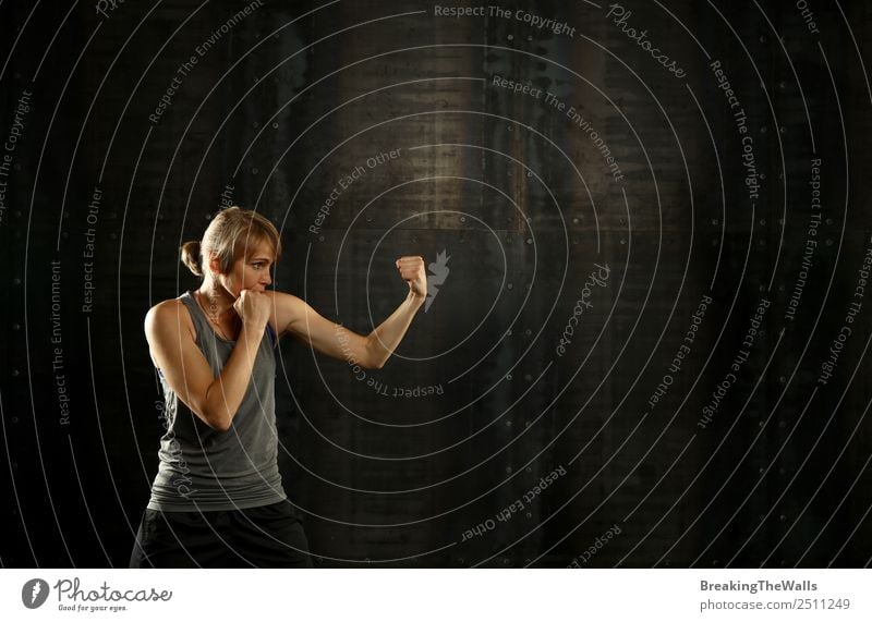 Close up side view profile portrait of one young middle age athletic woman shadow boxing in sportswear in gym over dark background, looking away Lifestyle