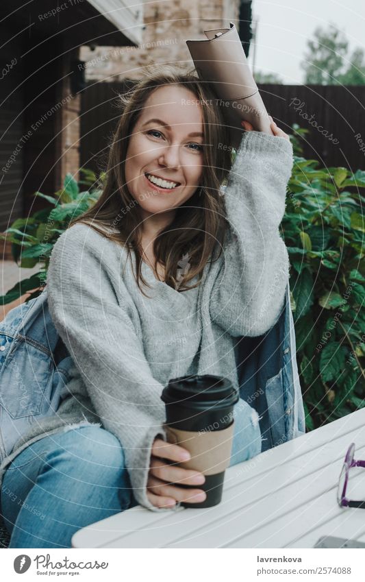 Lifestyle portrait of young female in grey sitting outdoors Rain hiding Covering Handbag Sweater Denim Jeans PDA Warmth Happy Relaxation Safety (feeling of)