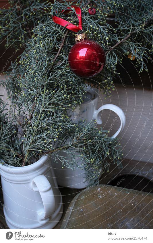 Nostalgic Christmas decoration with delicate fir branches, red bauble and vases on an old table. Red christmas bauble hangs shiny on twigs. Glowing Christmas bauble hanging from branches in old white nostalgic porcelain pots at home.