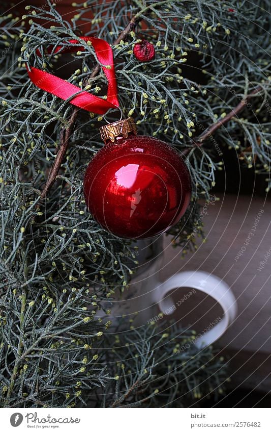 Nostalgic, festive Christmas decoration with delicate fir branches, red bauble and ribbon. Red Christmas bauble hangs shiny on branches. Shiny Christmas bauble hangs from branches in old white nostalgic porcelain pot at home.