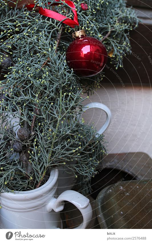 Nostalgic Christmas decoration with delicate fir branches, red bauble and vases on an old table. Red christmas bauble hangs shiny on twigs. Glowing Christmas bauble hanging from branches in old white nostalgic porcelain pots at home.