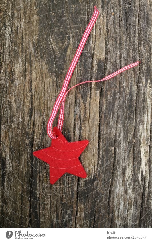 Merry Christmas. Red star of felt with ribbon, lies on old wood. Red checked Christmas star, as decoration on rustic brown wooden board. Felt fabric star as sign, blank, pendant, hanger on brown, rustic wooden table, text space.