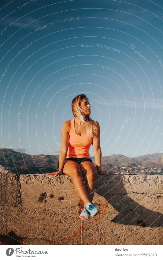 Beautiful woman with sports clothes, sitting on a concrete wall outdoors at sunset. Lifestyle Sun Mountain Sports Fitness Sports Training Human being Feminine