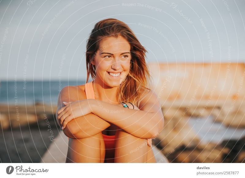 Beautiful woman with sports clothes, sitting on a concrete wall outdoors at sunset. Lifestyle Joy Body Wellness Relaxation Leisure and hobbies Sun Sports