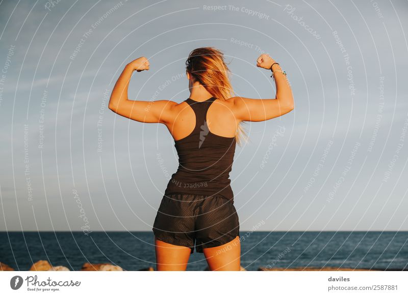 Young girl showing strong biceps after outdoors fitness workout. Fitness woman. Whole body back view. Joy Beautiful Body Athletic Summer Beach Sports