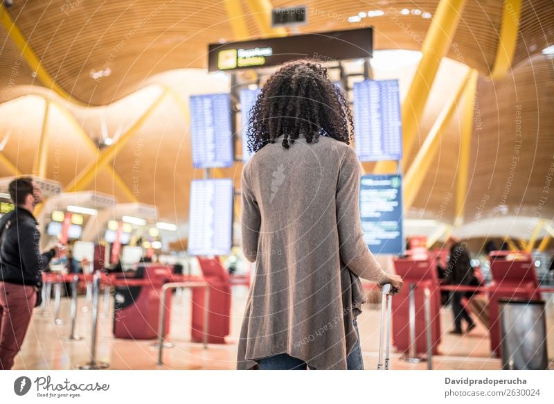 Black Woman looking at the timetable information panel in the airport with a suitcase Airport Timetable Display Human being Story Board International