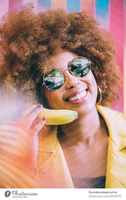 Surprised mixed race woman in a colorful artwork background wall playing with a banana Woman Mixed Close-up Portrait photograph Black Cheerful Banana Yellow