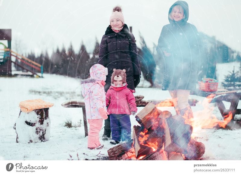 Family spending time together outdoors in the winter. Parents with children gathered around the campfire preparing marshmallows and snacks to toasting over the campfire using wooden sticks