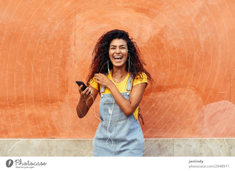 Young Arab woman laughing and listening to music with earphones outdoors Lifestyle Hair and hairstyles Telephone Technology Human being Feminine Young woman