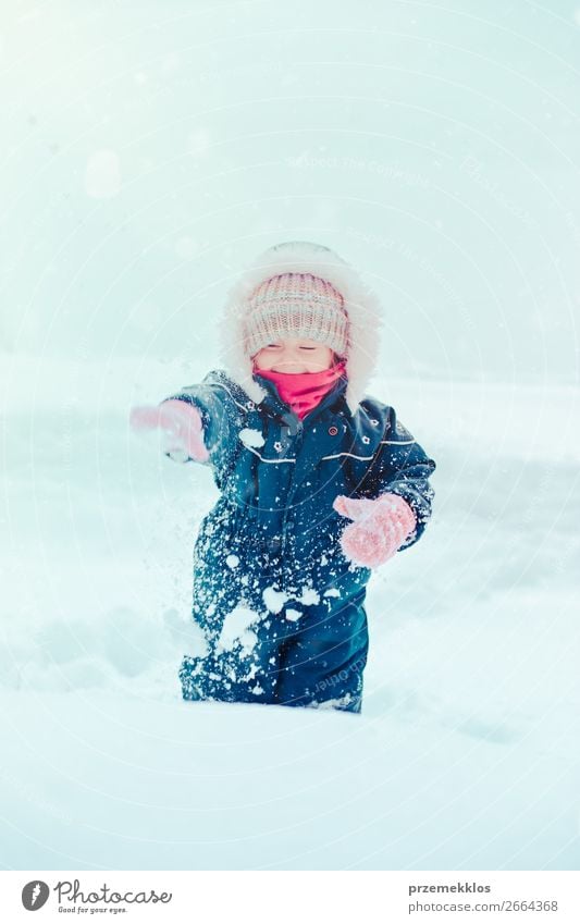 Happy little girl enjoying snow. Child playing outdoors walking through deep snow in wintertime while snow falling. Toddler is wearing dark blue snowsuit