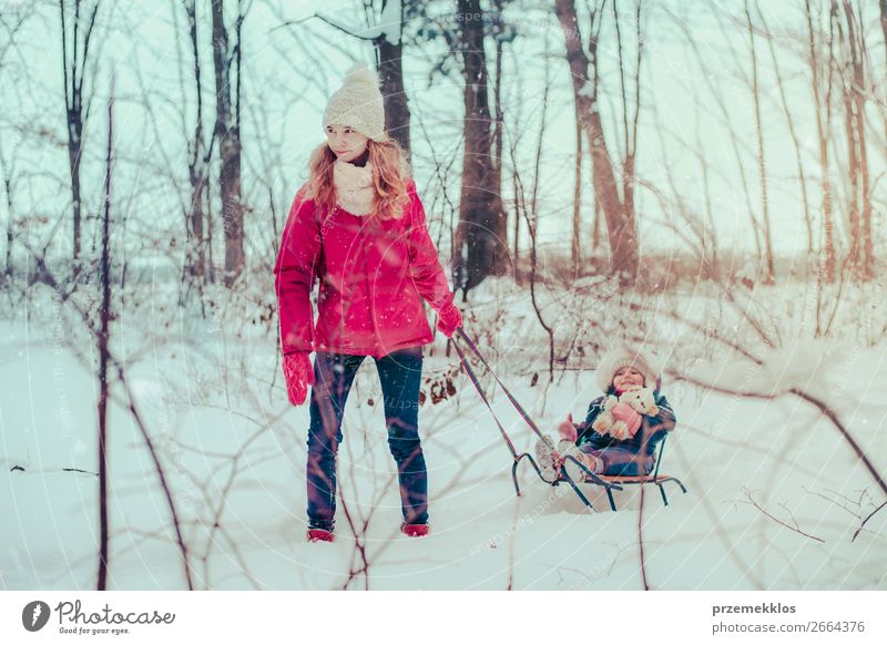 Teenage girl pulling sled with her little sister through forest Lifestyle Joy Happy Winter Snow Winter vacation Human being Child Baby Toddler Girl Young woman