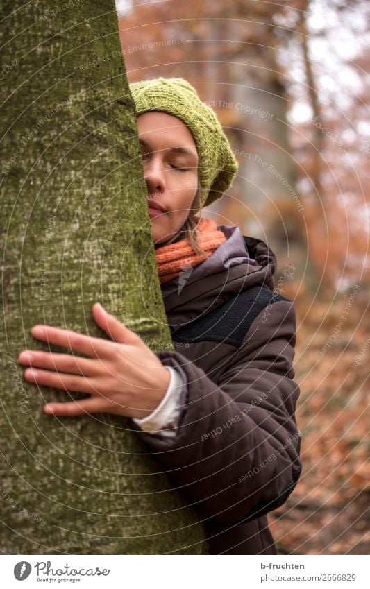 Woman with wool cap, scarf and winter coat hugs tree Senses Relaxation Calm Meditation Adults Face by hand Autumn Park Forest Touch Stand Dream Embrace natural