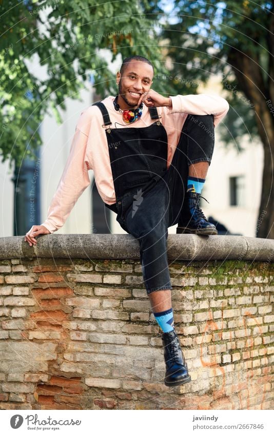 Young black man wearing casual clothes and headphones sitting on urban background. Lifestyle Happy Beautiful Human being Masculine Young man