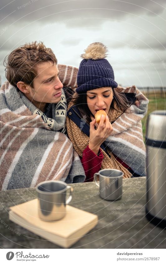 Young couple under blanket eating muffin outdoors in a cold day Eating Beverage Coffee Tea Lifestyle Adventure Ocean Winter Table Woman Adults Man Couple Nature