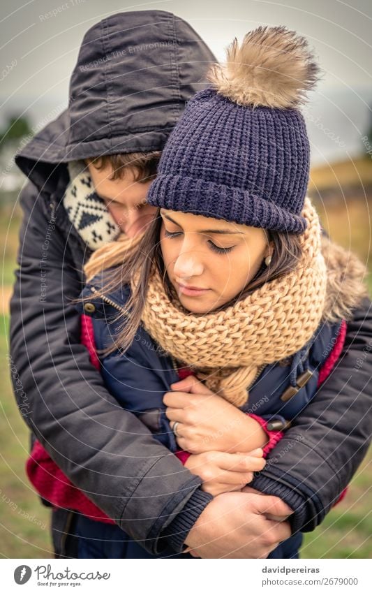 Young couple with hat and scarf embracing outdoors Lifestyle Happy Beautiful Winter Woman Adults Man Couple Nature Sky Clouds Autumn Wind Warmth Clothing Scarf